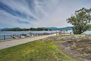 A lakeside walkway with a stone bench, a gazebo, and a view of the lake and mountains.