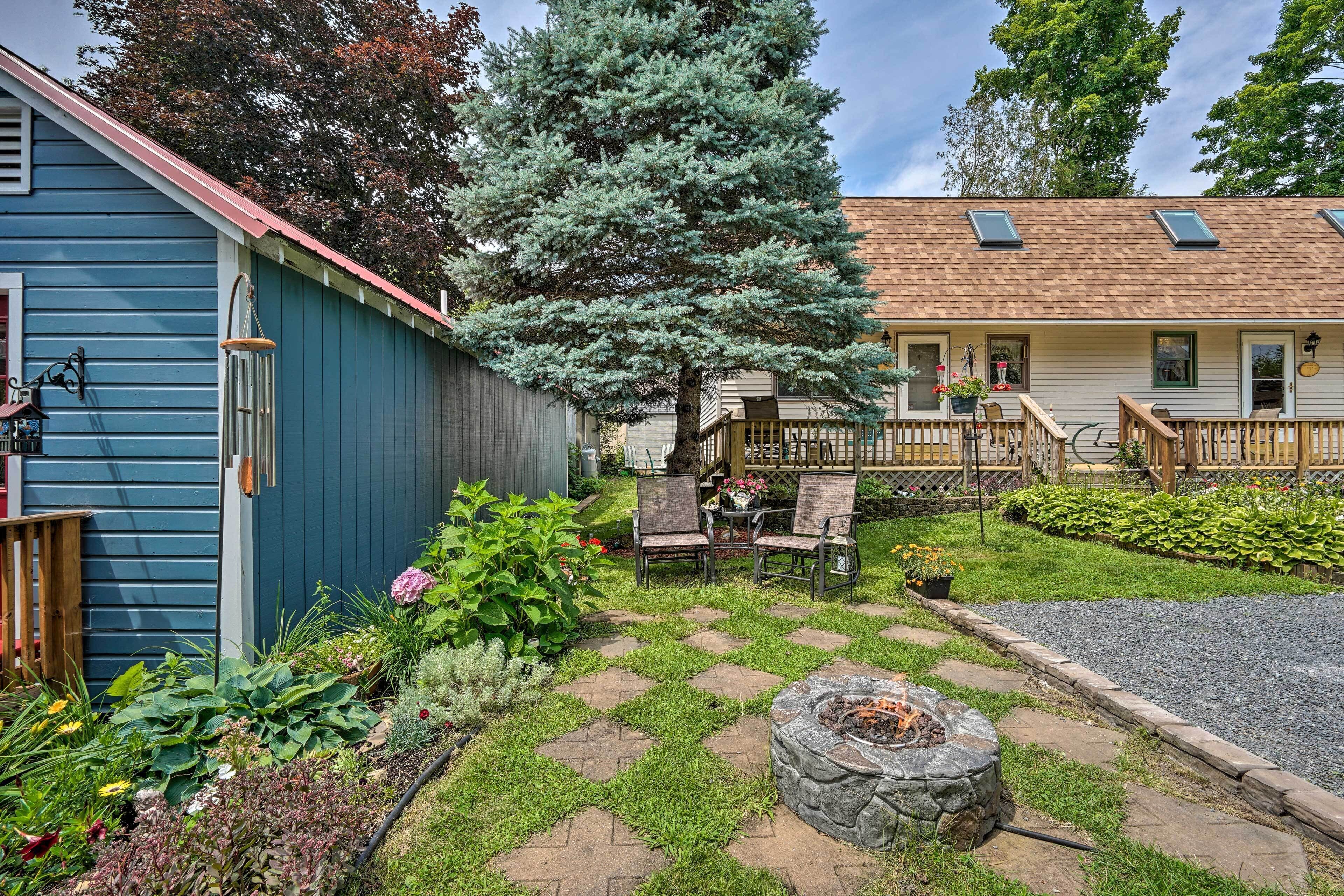 Une maison bleue avec un foyer extérieur, une terrasse en bois et un jardin où poussent différentes espèces de plantes.