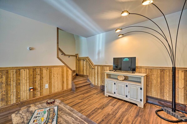 A room with wooden flooring, a staircase, a television on a cabinet, and a floor lamp.