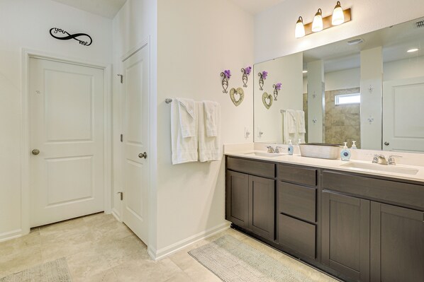 A bathroom with a double vanity, white walls, a large mirror, and decorative heart-shaped wall art.