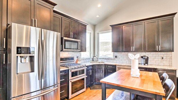A modern kitchen with stainless steel appliances, dark wood cabinets, and a wooden dining table. - Alma Retreat w/ Mtn Views ~ 17 Mi to Breck! (Alma)