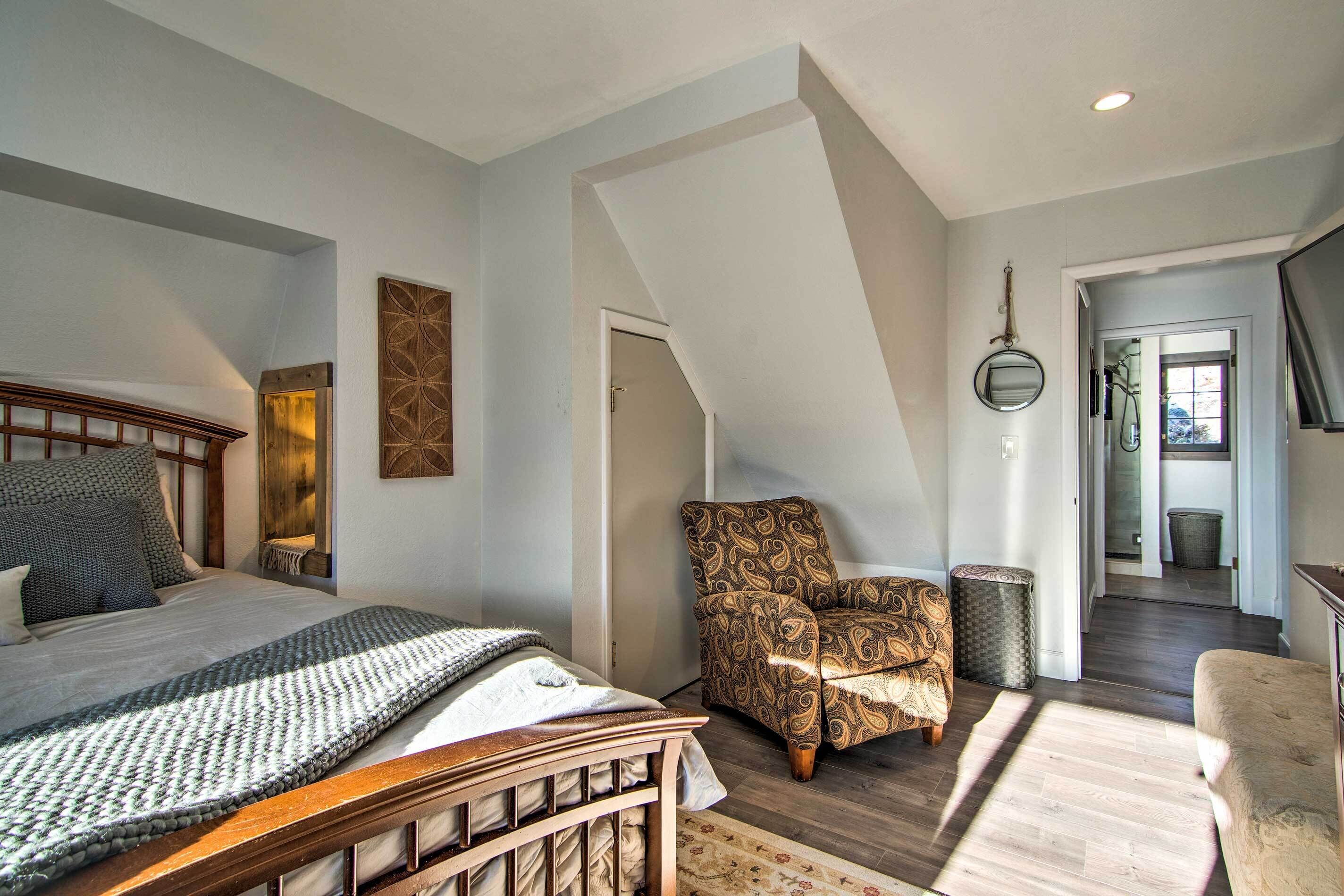 A bedroom with a wooden bed, a patterned armchair, and a view of the hallway.