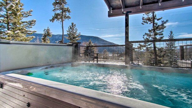 A hot tub with a wooden deck, surrounded by trees and a mountain view. - Outdoor Kitchen & Swim Spa: 1-acre Grand Lake Home (Grand Lake)