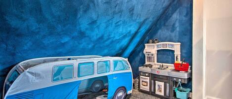 A room with a van-shaped bed, a kitchenette, and a patterned floor.