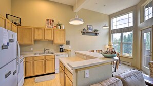 A kitchen with wooden cabinets, a white refrigerator, a built-in island, and a dining area with a brown leather couch. - Silverthorne Gem w/ Community Perks: 11 Mi to Ski! (Silverthorne)