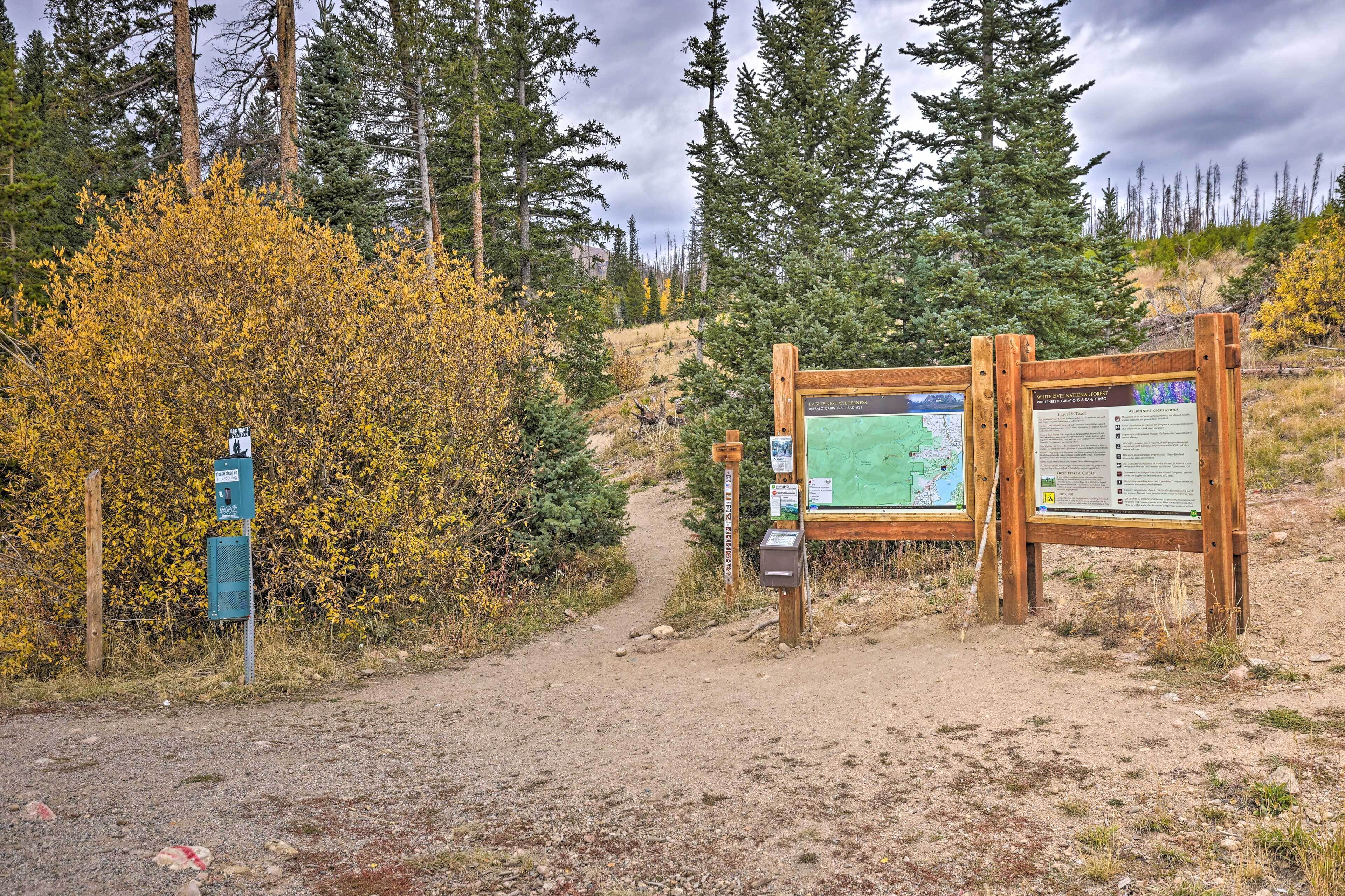 Un cartel de madera con mapas y paneles informativos, un sendero de tierra y árboles circundantes.