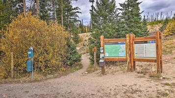 Un cartel de madera con mapas y paneles informativos, un sendero de tierra y árboles circundantes.