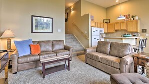 A living room with two sofas, a coffee table, and a lamp. There is a staircase leading to a kitchen area with wooden cabinets and a refrigerator. - Silverthorne Gem w/ Community Perks: 11 Mi to Ski! (Silverthorne)
