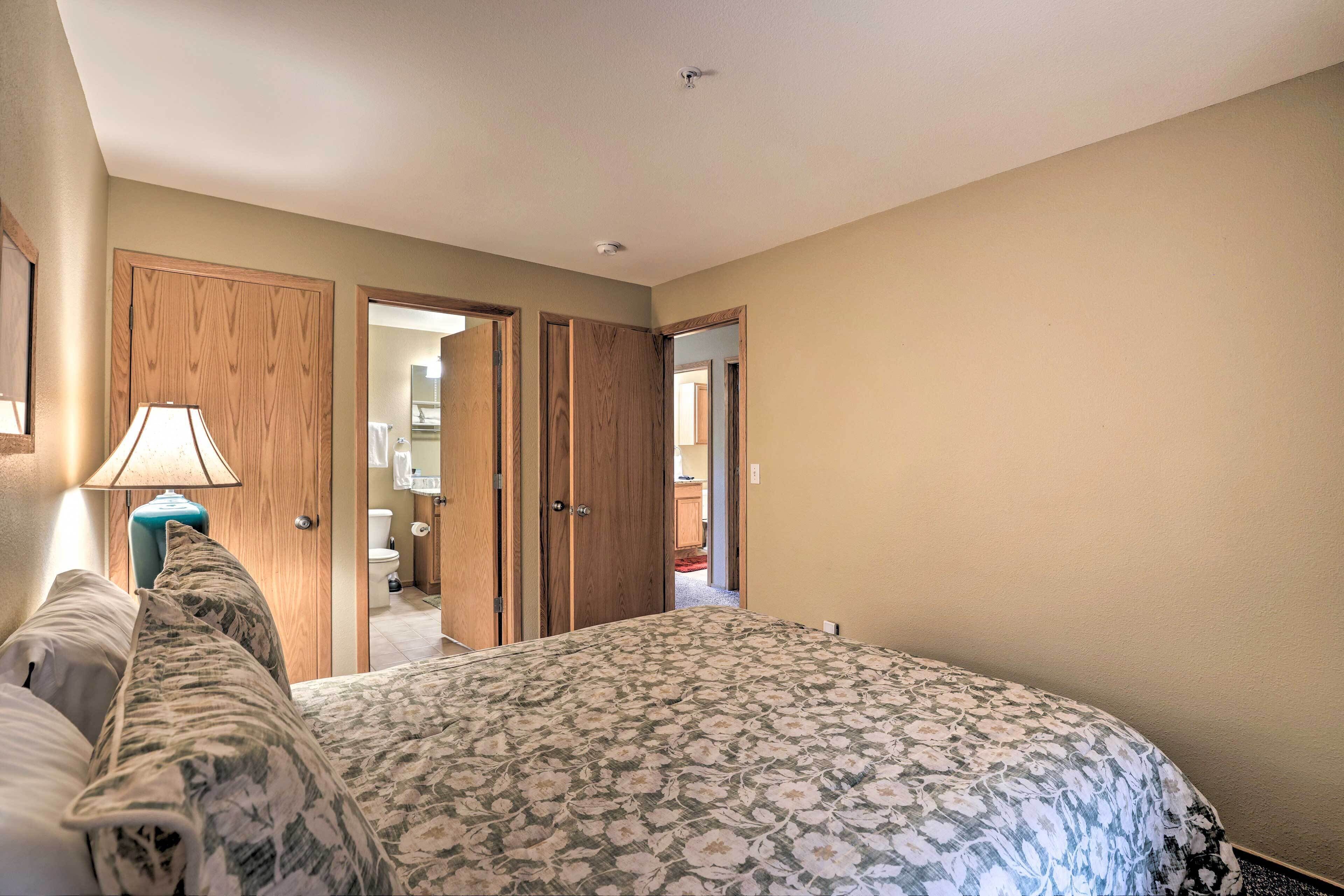 A bedroom with a floral bedspread, wooden wardrobe, and a nightstand with a lamp.