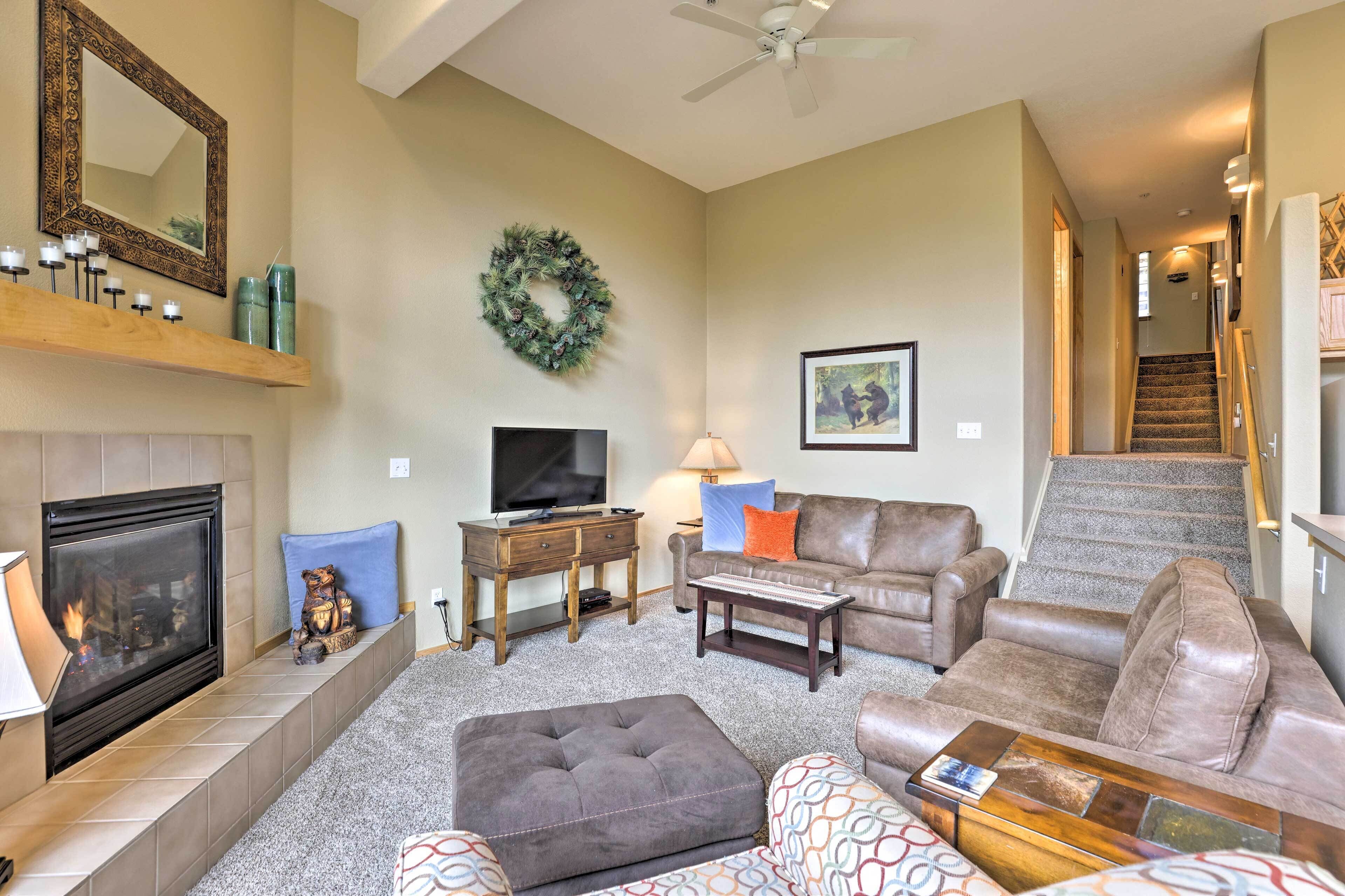 A living room with a fireplace, television, sofa, ottoman, and a staircase leading to another level.