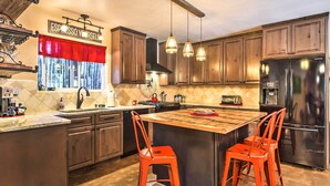 A kitchen with wooden cabinets, a central island with stools, pendant lighting, and a stainless steel refrigerator.