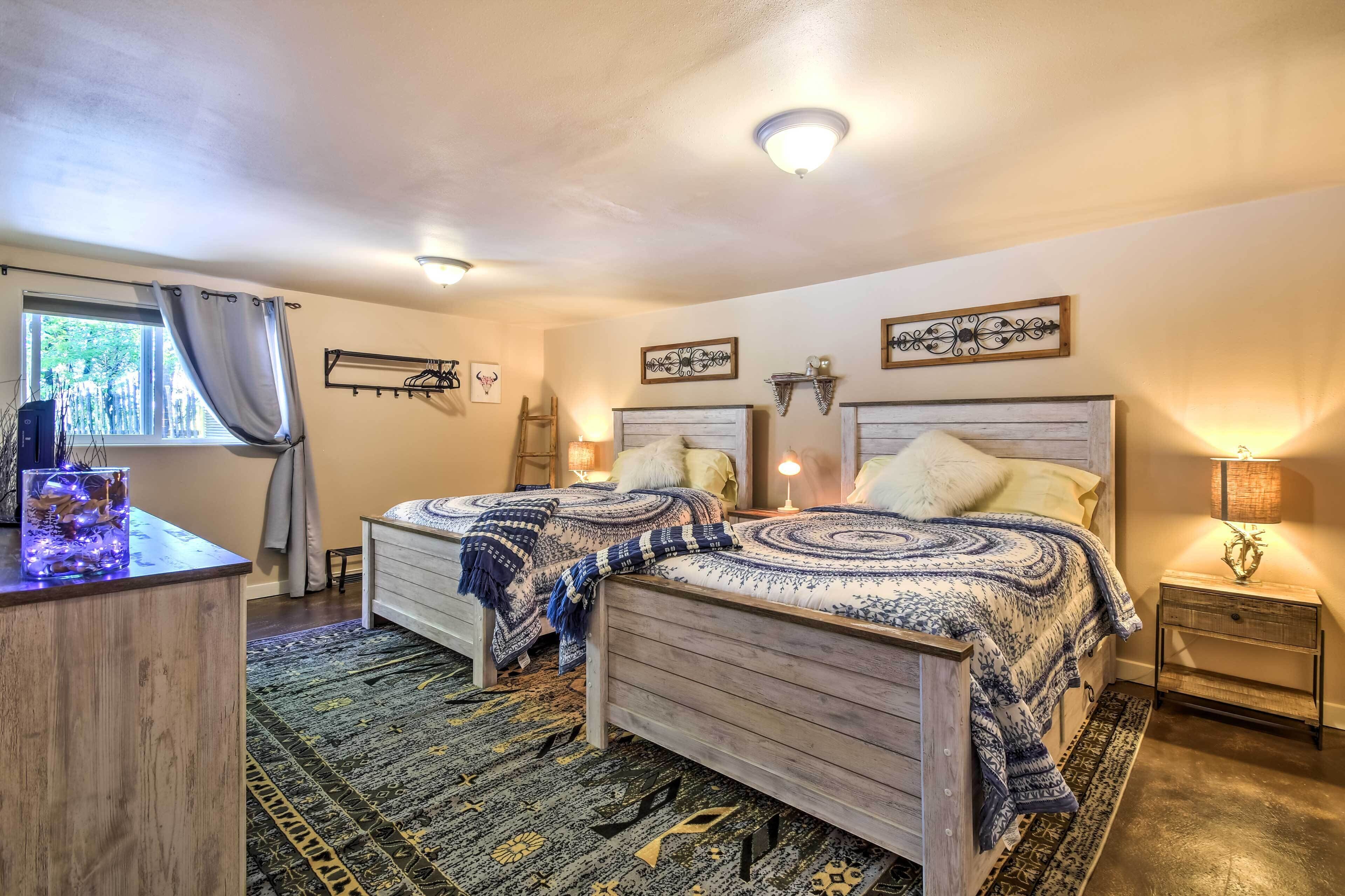 A bedroom with two wooden beds, a nightstand, a lamp, a window with curtains, and a decorative wall piece.