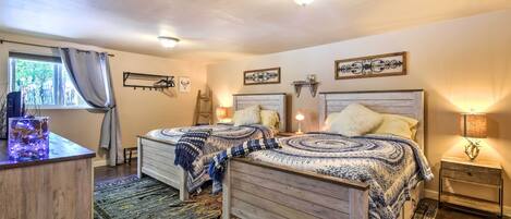 A bedroom with two wooden beds, a nightstand, a lamp, a window with curtains, and a decorative wall piece.
