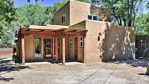 A rustic building with a covered patio area, a wooden pergola, and a dirt ground.