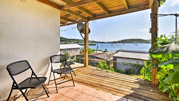 A covered patio with two black metal chairs, a satellite dish, and a view of a body of water and hills in the distance. - Tropical Oasis: Bay Views ~ 2 Mi to Playa Sardinas (Culebra)