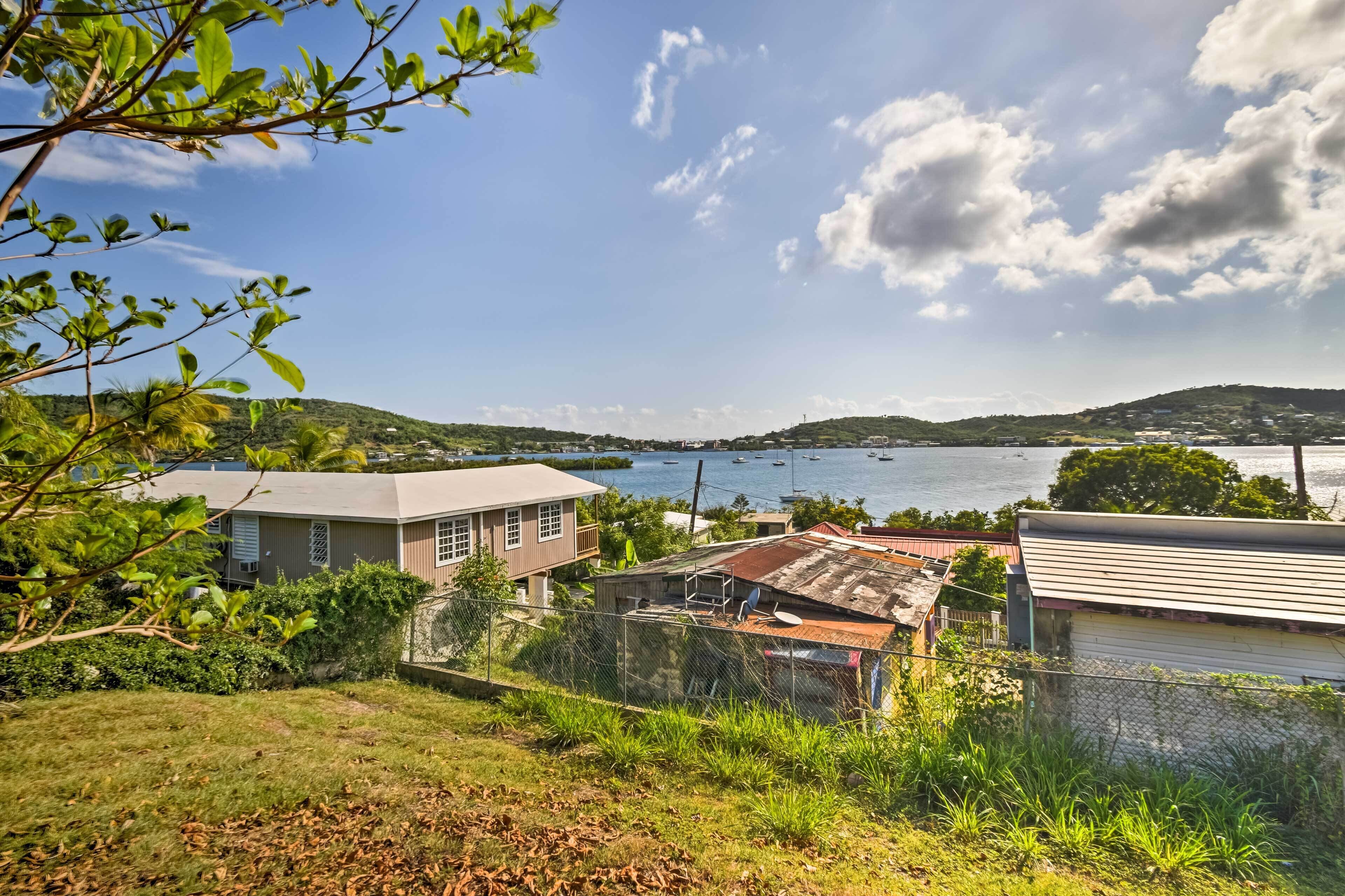 Zona residencial costera con casas, una colina cubierta de césped y vistas al mar con barcos.