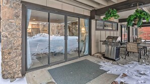 A covered patio area with a stone wall, a sliding glass door, a barbecue grill, and outdoor furniture. - Ski-in/ski-out Condo w/ Hot Tub on Copper Mountain (Copper Mountain)