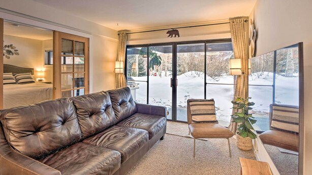 A cozy living room with a leather sofa, a coffee table, and a view of a snowy outdoor area through large glass doors. - Ski-in/ski-out Condo w/ Hot Tub on Copper Mountain (Copper Mountain)