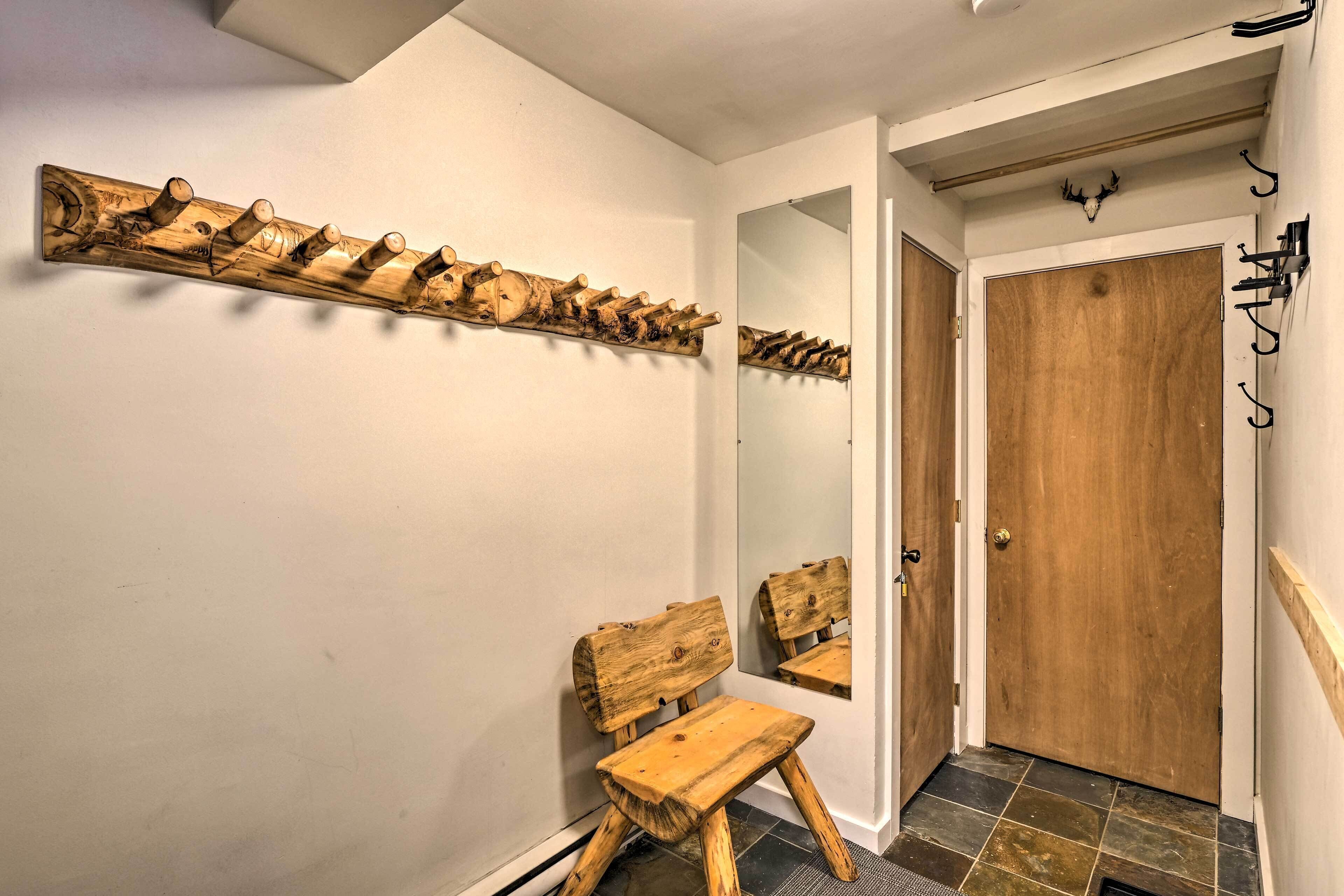 A wooden bench and a coat rack in a hallway with a wooden door and a mirror.