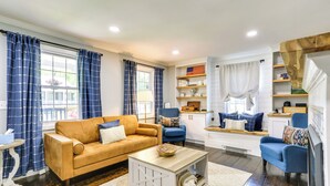 A living room with a sofa, armchairs, a coffee table, and a kitchen area with a window, curtains, and shelves. - Bright Cornwall-on-hudson Vacation Rental! (Cornwall)