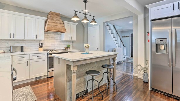 A modern kitchen with white cabinets, a central island with stools, a stainless steel refrigerator, and a staircase leading to another level. - Bright Cornwall-on-hudson Vacation Rental! (Cornwall)