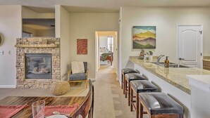 A modern kitchen with a stone fireplace, a dining area with a wooden table, and a bar with stools. - Ski, Hike & Golf: Granby Condo w/ Shared Amenities (Granby)
