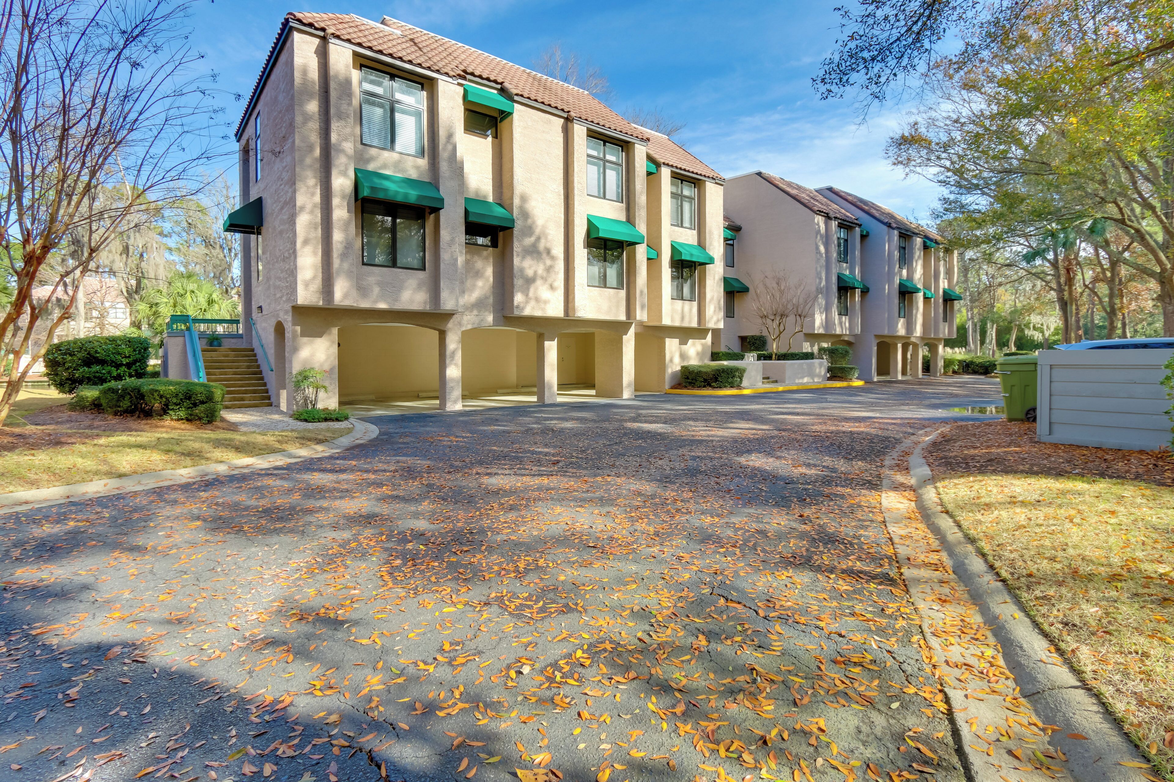A residential building with a driveway covered in fallen leaves, a gated entrance, and a well-maintained lawn.