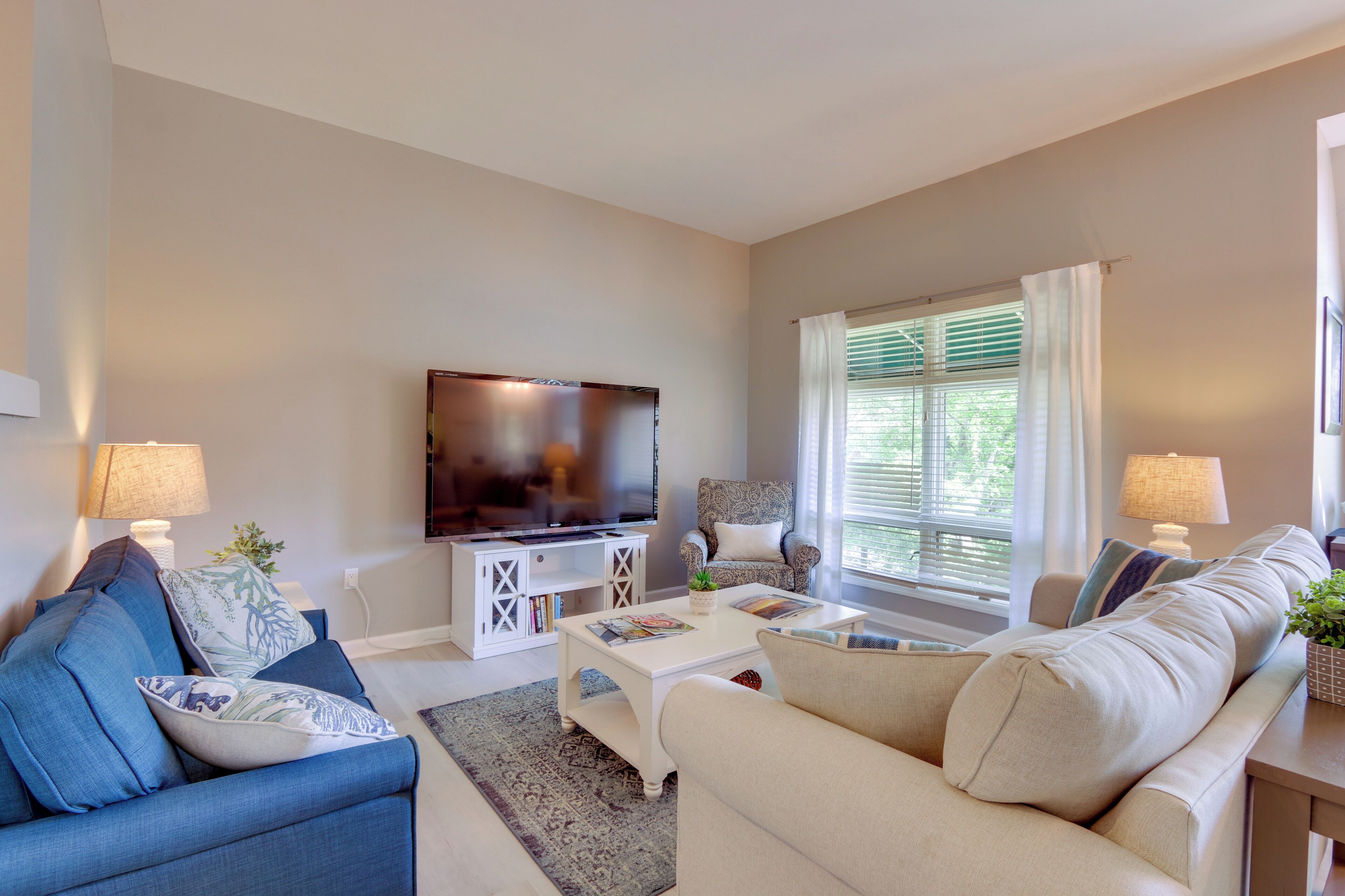 A living room with a TV, two sofas, a coffee table, and a window with curtains.