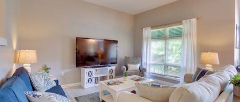 A living room with a TV, two sofas, a coffee table, and a window with curtains.