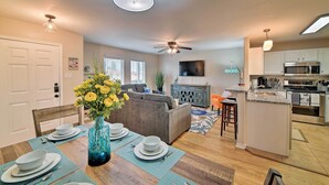A modern kitchen with a microwave, stove, and island counter. There is a dining area with a table set for four, a sofa, and a vase with flowers. - Corpus Christi Condo w/ Pool Access, Walk to Beach (Corpus Christi)