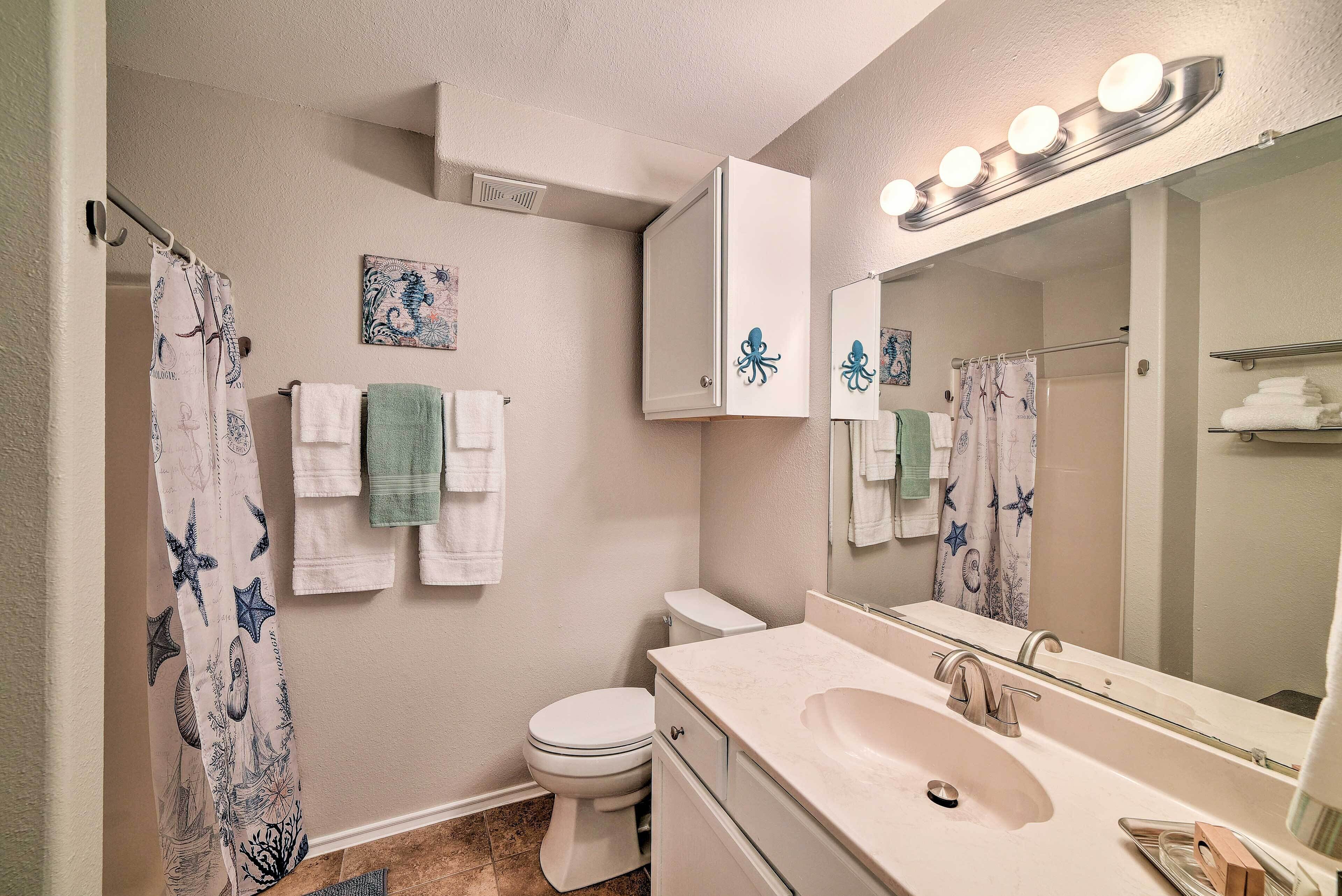 A bathroom with a white sink, a toilet, a shower curtain with a starfish design, and a mirror with lights above it.