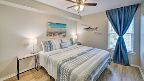 A bedroom with a bed, a nightstand, a ceiling fan, a window with curtains, and a wall with a shark decal. - Corpus Christi Condo w/ Pool Access, Walk to Beach (Corpus Christi)