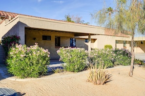 A stucco building with a tiled roof, a covered entrance, and a landscaped garden with pink flowering plants. - Golf Course View & Pool Access: Palm Desert Condo (Palm Desert)