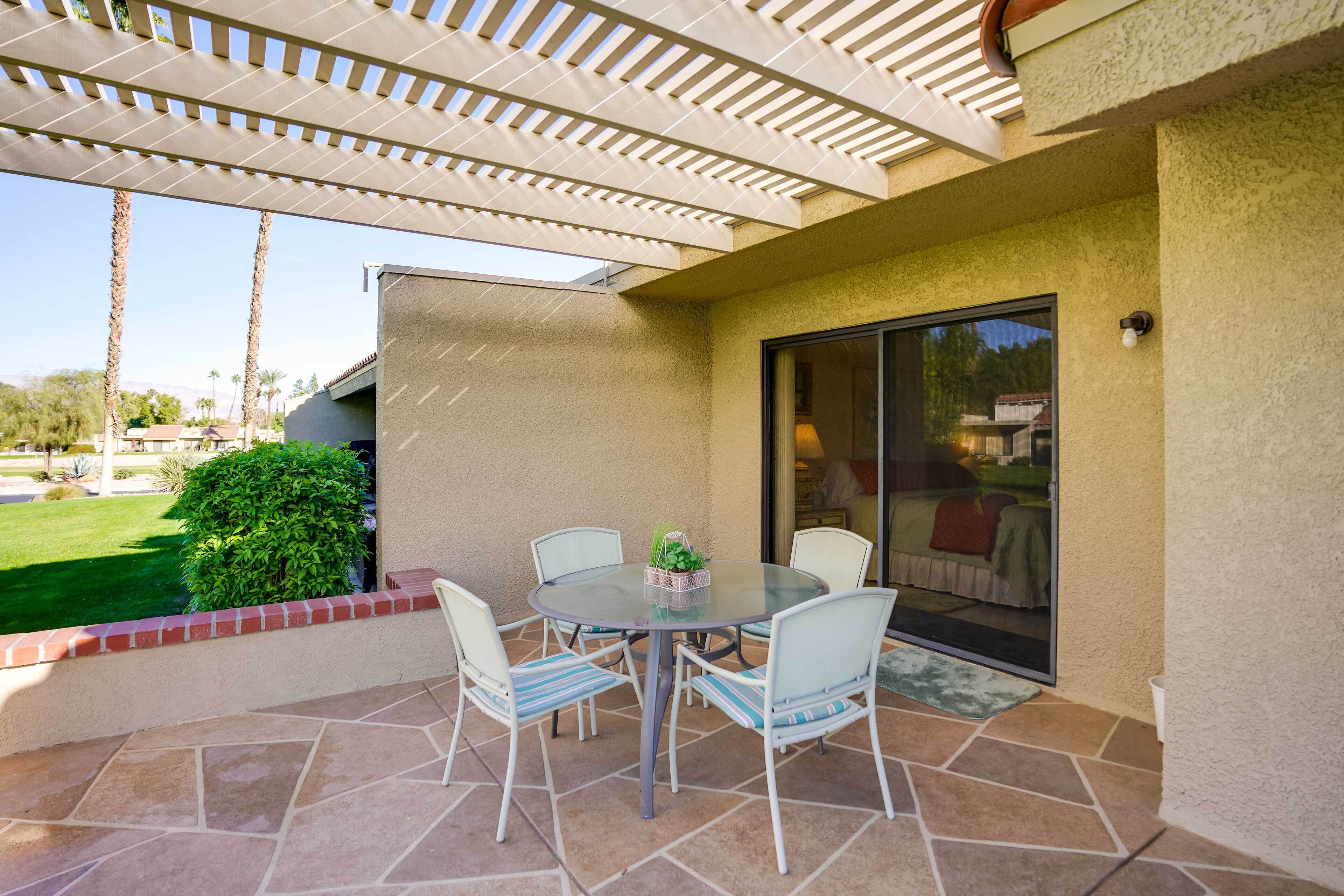 An outdoor patio with a round table and chairs, a pergola overhead, and a view of a residential area.