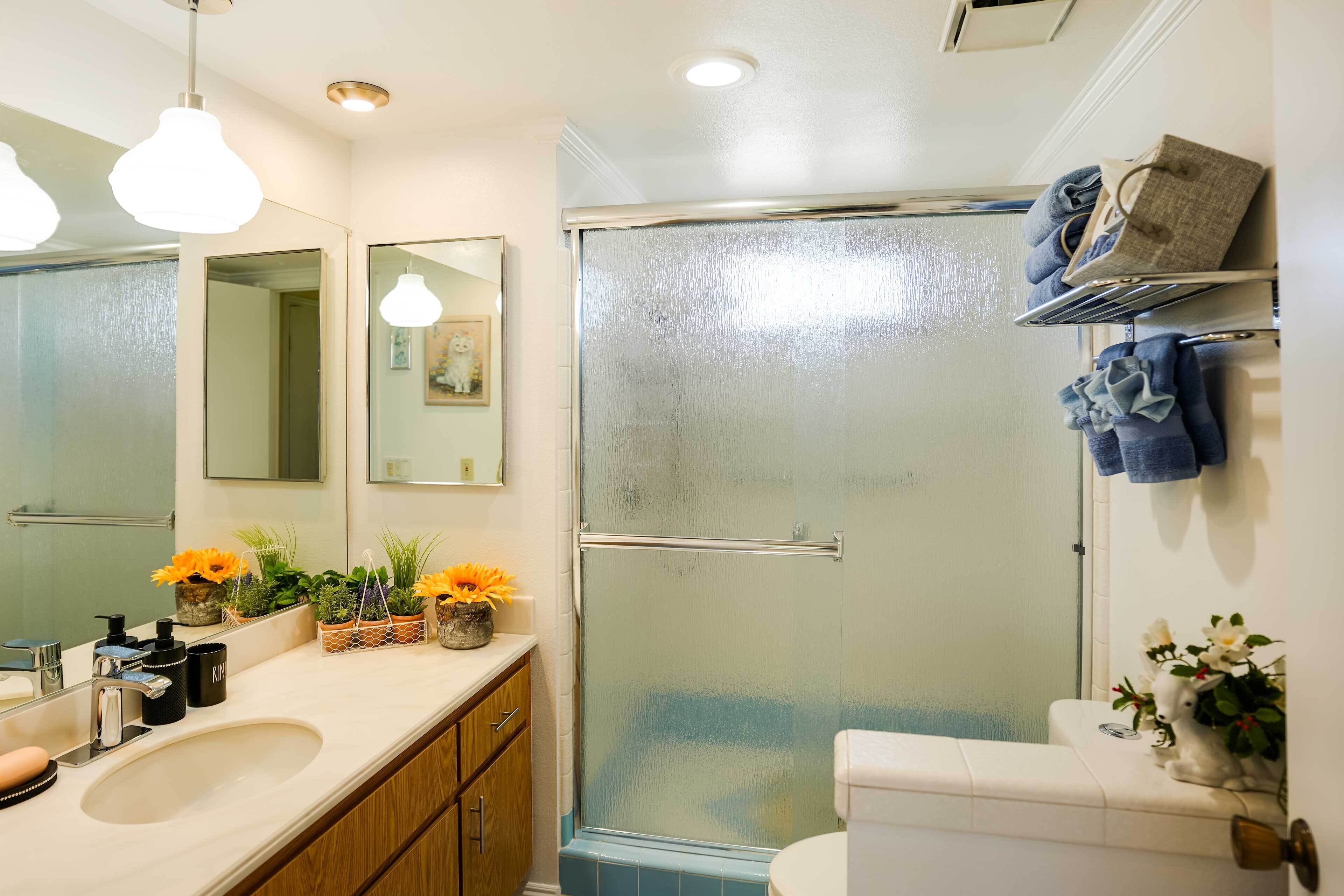 Une salle de bain avec un lavabo blanc, un miroir et des toilettes, une douche avec une porte en verre et un porte-serviettes avec des serviettes.