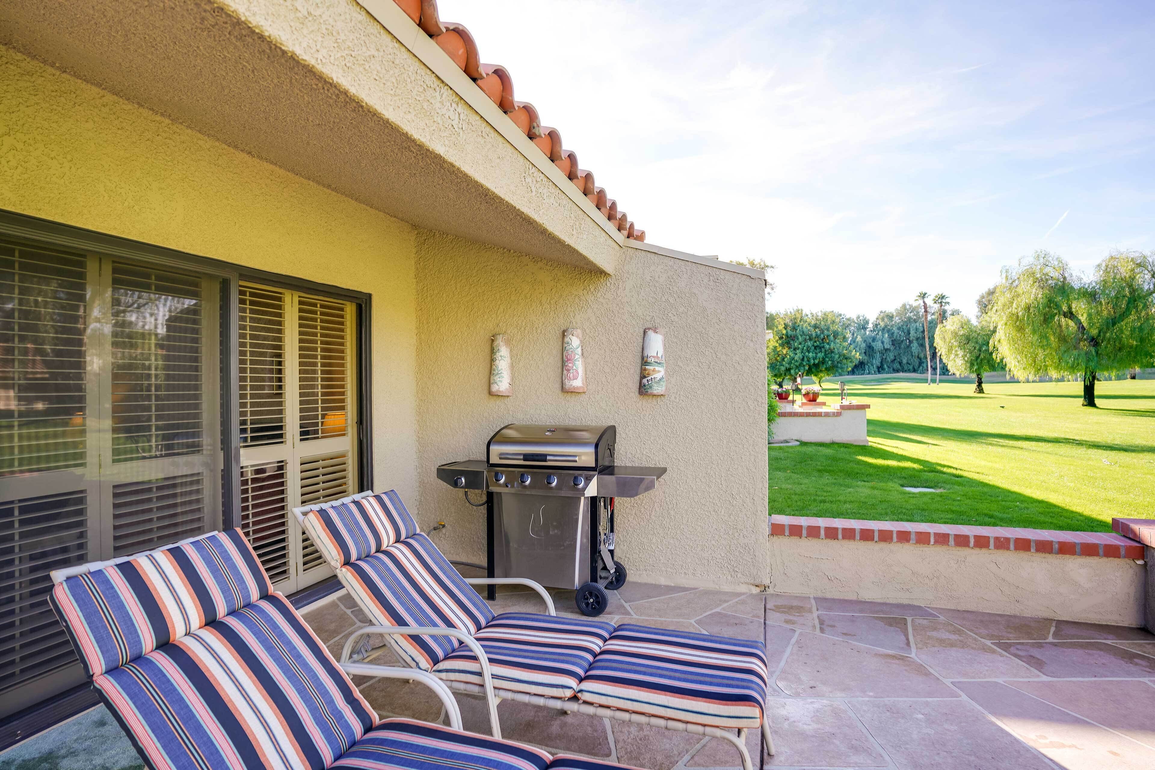 A patio with two striped lounge chairs, a grill, and a view of a well-maintained lawn.