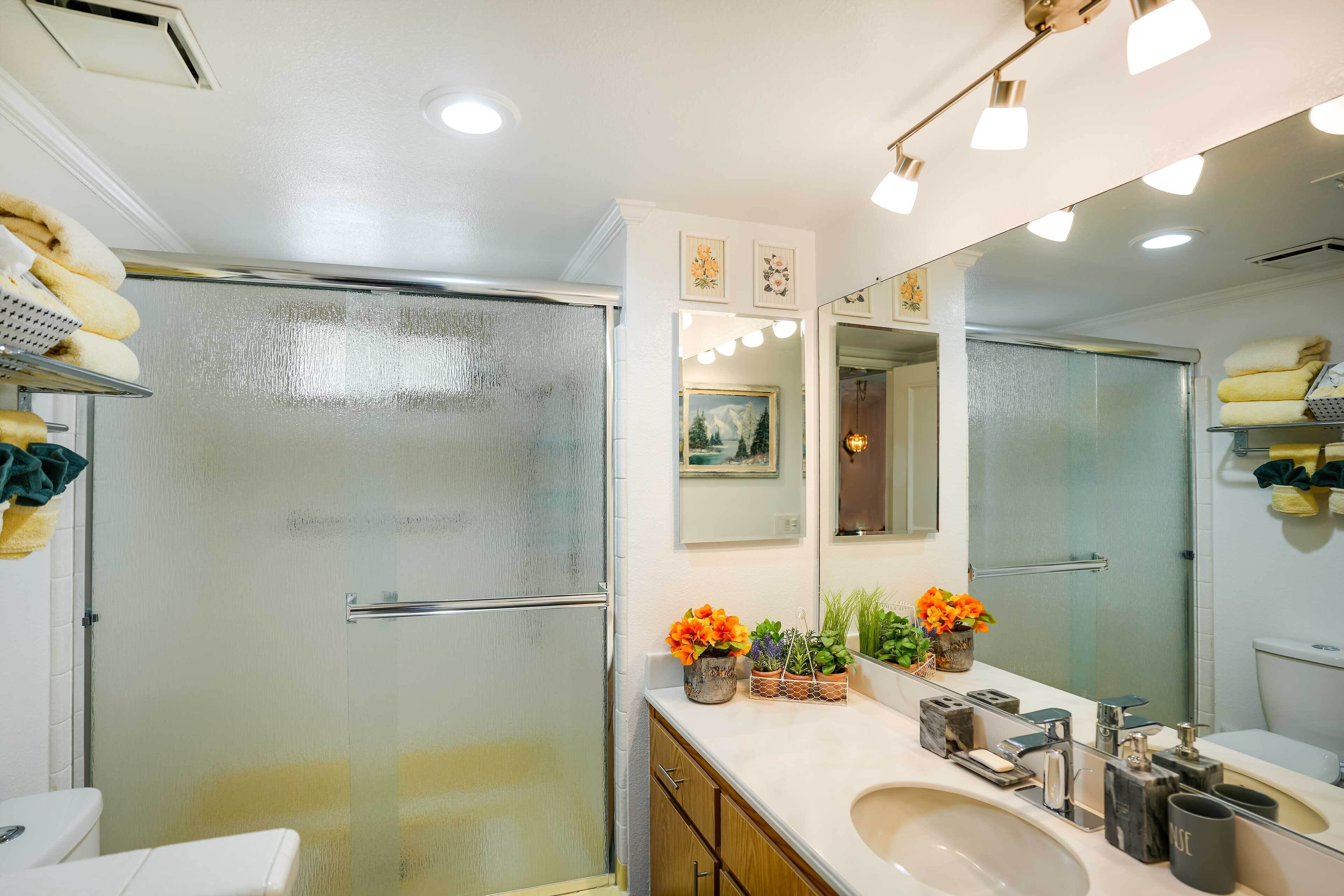 Une salle de bain moderne avec une porte de douche en verre, un lavabo blanc et un grand miroir.
