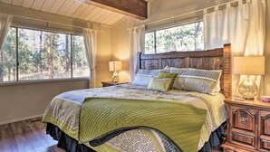 Quarto com cama grande, cabeceira de madeira e vista para árvores pela janela.