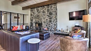 Uma sala de estar moderna com parede de pedra, sofás de couro, lareira e televisão de tela plana.
