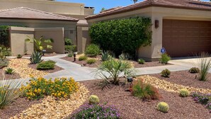 Zona residencial amb una entrada, un garatge i diversos jardins ben cuidats, que inclouen cactus i plantes amb flors.