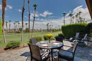 Une terrasse extérieure avec une table ronde et des chaises, donnant sur un terrain de golf bordé de palmiers.