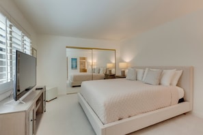 Une chambre à coucher moderne avec un grand lit, un téléviseur posé sur un meuble et un miroir.
