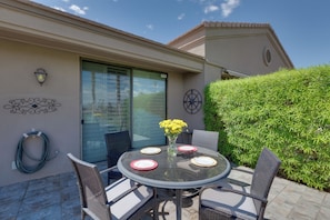 An outdoor patio with a round glass table, wicker chairs, and a vase with yellow flowers. - Beautiful Gated Country Club, Prime Location (Palm Desert)