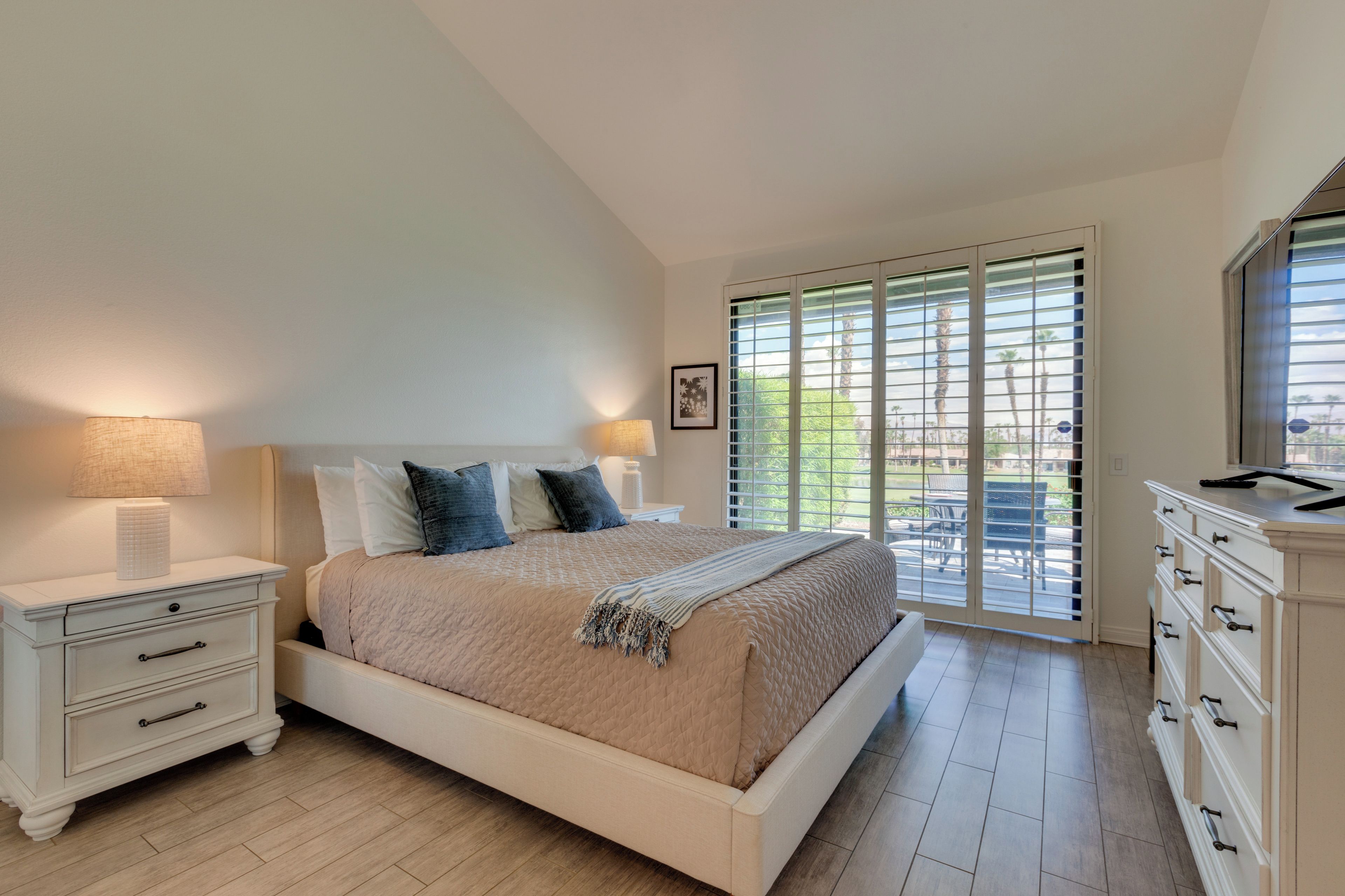 A bedroom with a bed, bedside tables, a dresser, and a view through a window.
