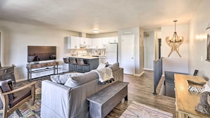 A modern living room with a grey sofa, a wooden coffee table, and a TV. There is a kitchen area with white cabinets and a dining table with chairs. - 7 Mi to Keystone: Mtn-view Abode w/ Deck! (Dillon)