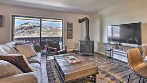 A cozy living room with a large window, a fireplace, a TV, and comfortable seating. - 7 Mi to Keystone: Mtn-view Abode w/ Deck! (Dillon)