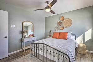 Quarto com cama, ventoinha no teto, penteadeira, espelho e arte decorativa na parede.