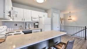 A modern kitchen with white cabinets, a large island, and a dining area with a bar stool. - 7 Mi to Keystone: Mtn-view Abode w/ Deck! (Dillon)