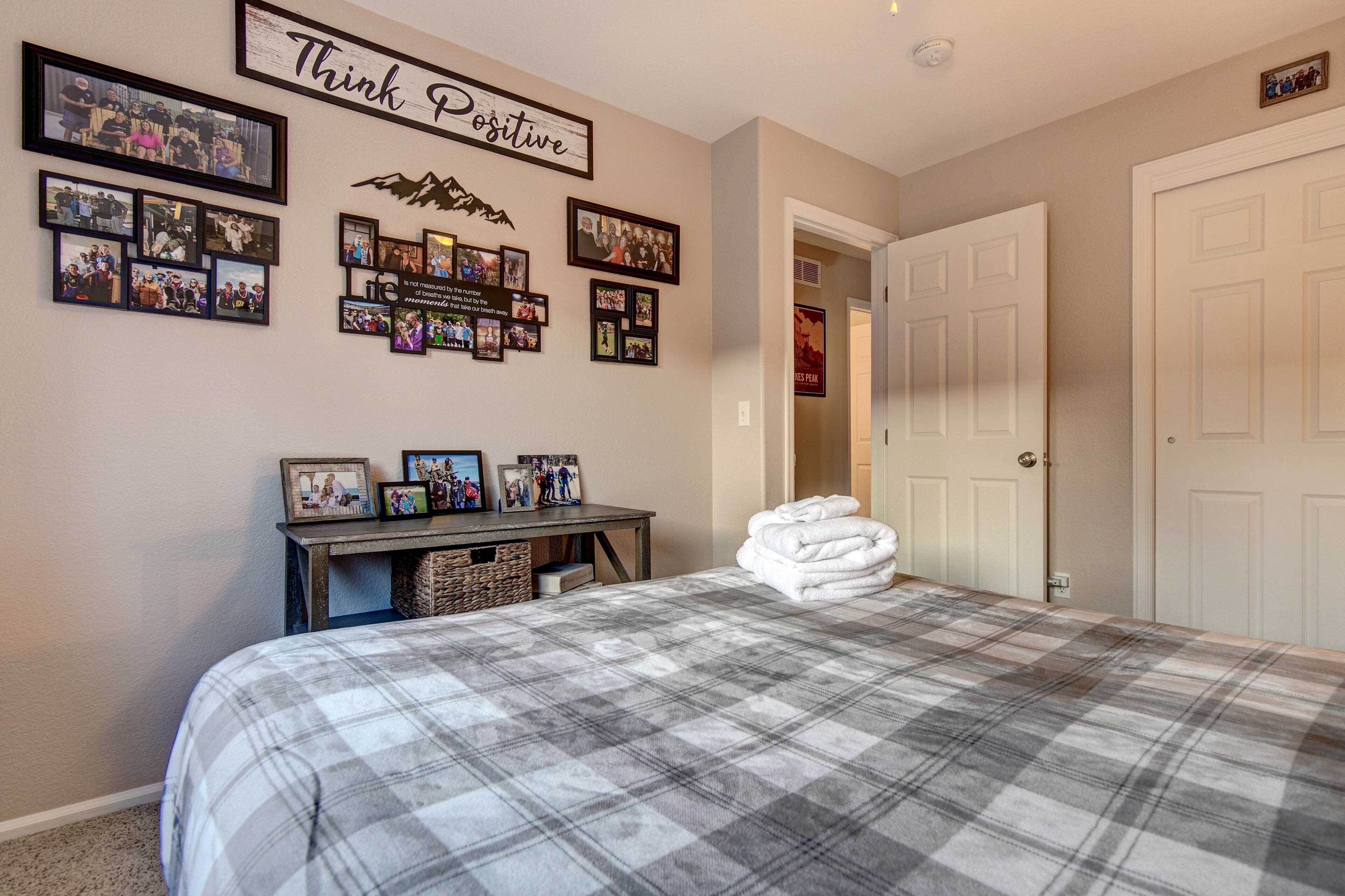 A bedroom with a bed, a wall with framed photos, a sign saying 'Think Positive', and a door.
