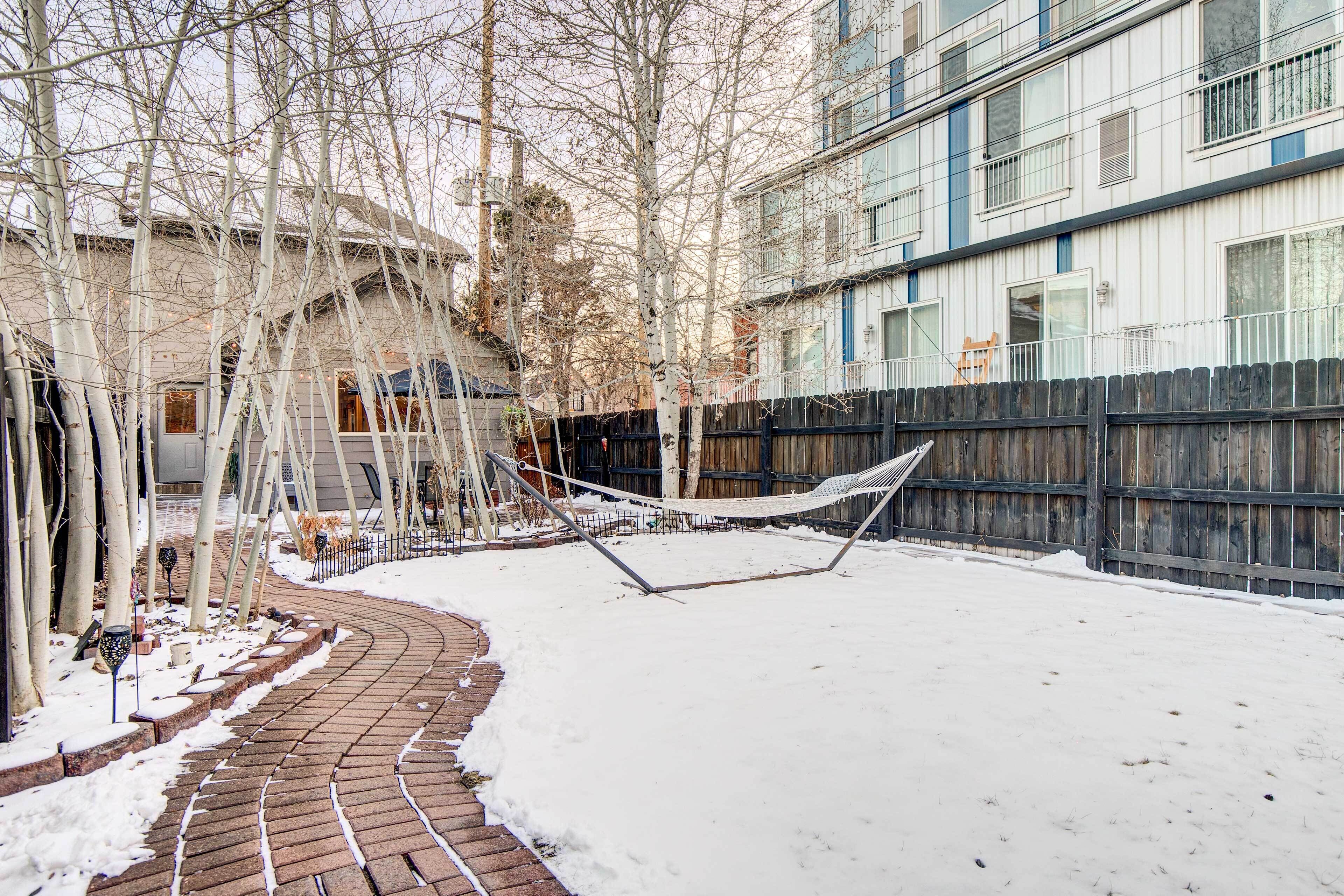 A snow-covered courtyard with a brick pathway, a hammock, and a wooden fence.